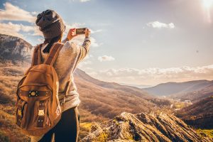 Photo of young girl with a backpack discovering the nature and making photos with smartphone
